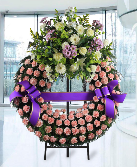 Corona funeraria con aro de claveles rosados con una cinta funeraria y cabezal superior con flores