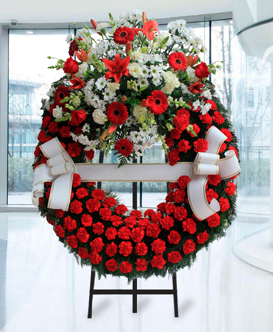 Corona funeraria con aro de claveles rojos y cabezal superior con flores blancas y rojas